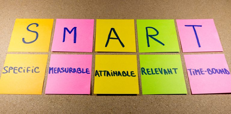 set goals SMART (specific, measurable, attainable, recorded, timely) colorful sticky notes on cork bulletin board